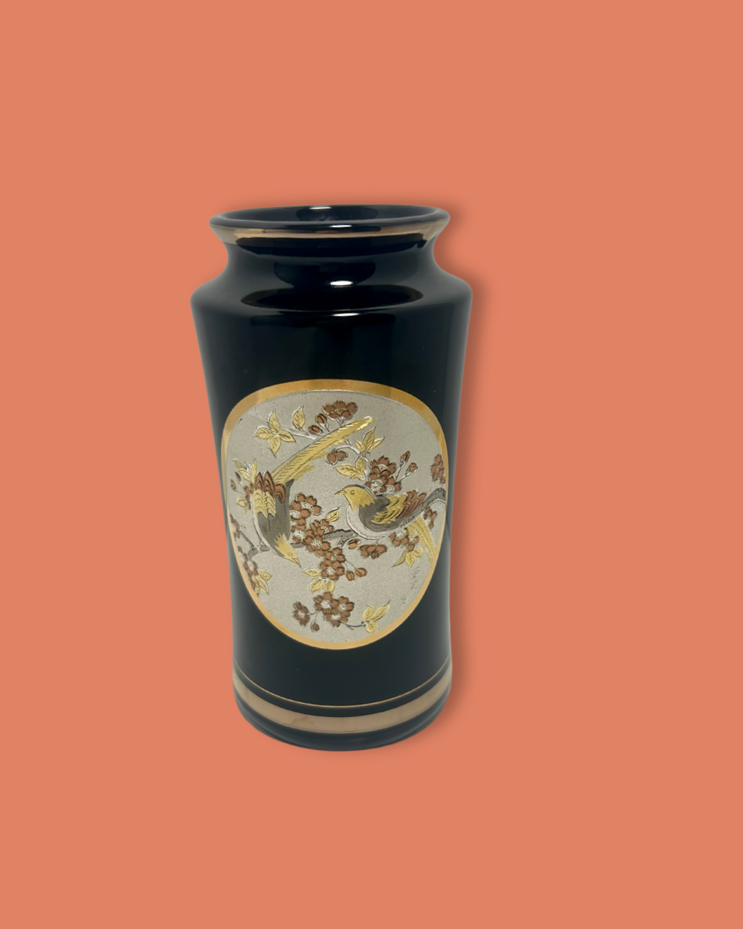 Black vase with decorative circular emblem on a peach background