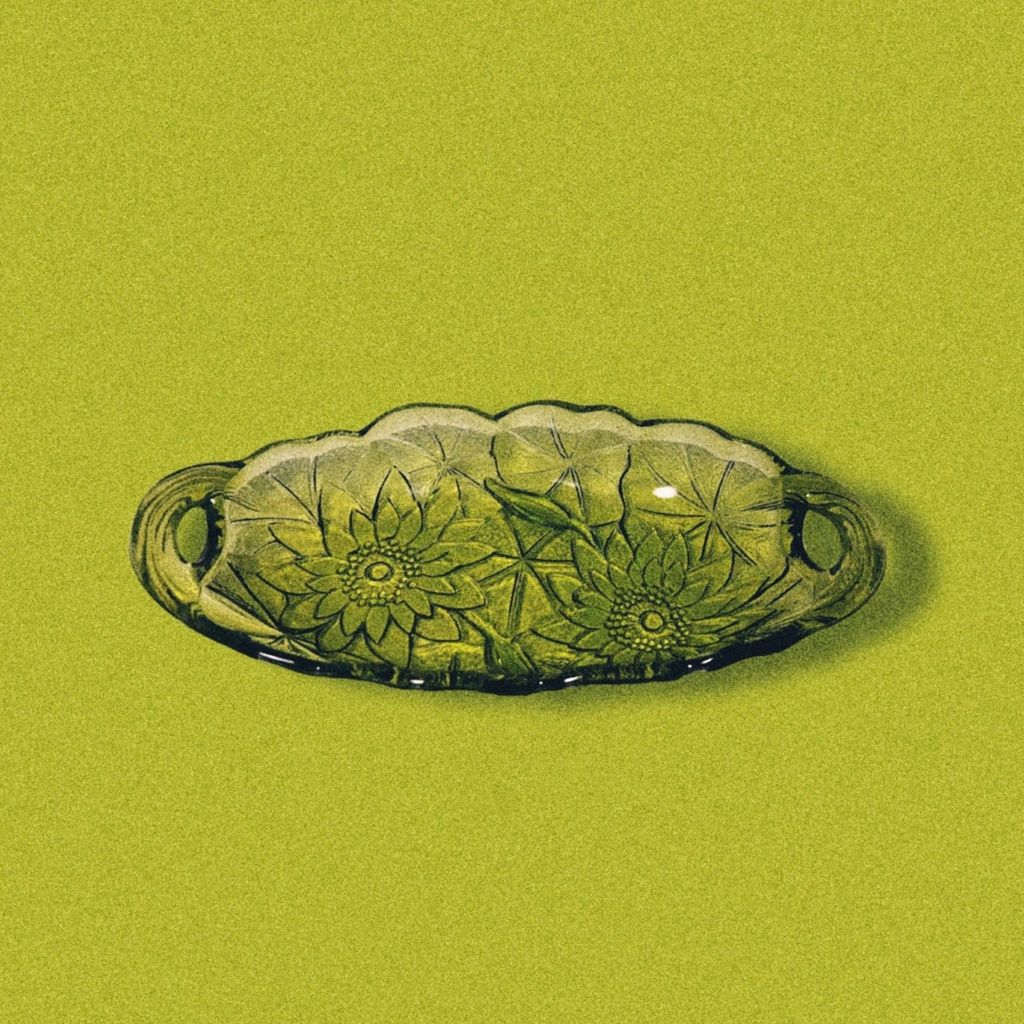 Avocado green glass candy dish with a sunflower pattern on a green background.
