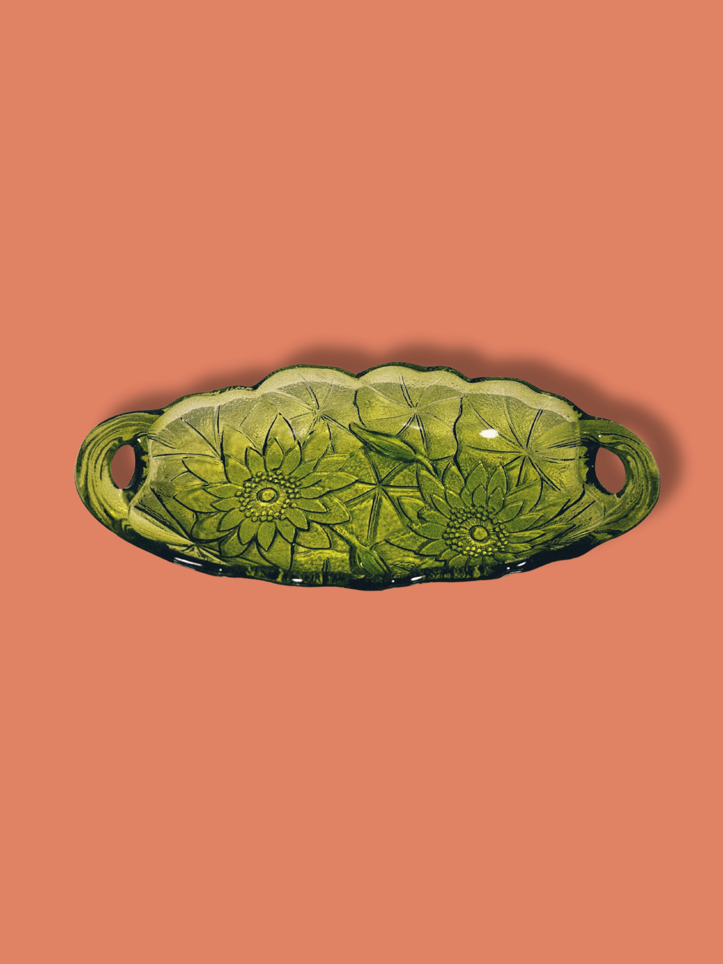 Avocado green glass candy dish with a sunflower pattern on an orange background.