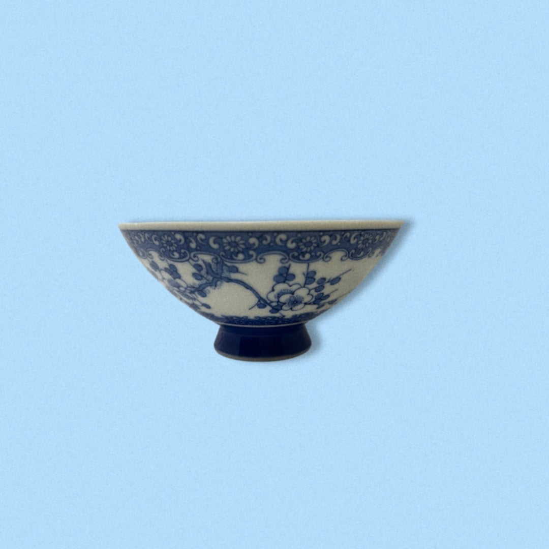 A vintage handpainted blue porcelain Japanese rice bowl with floral patterns on a white background, displayed against a blue background.