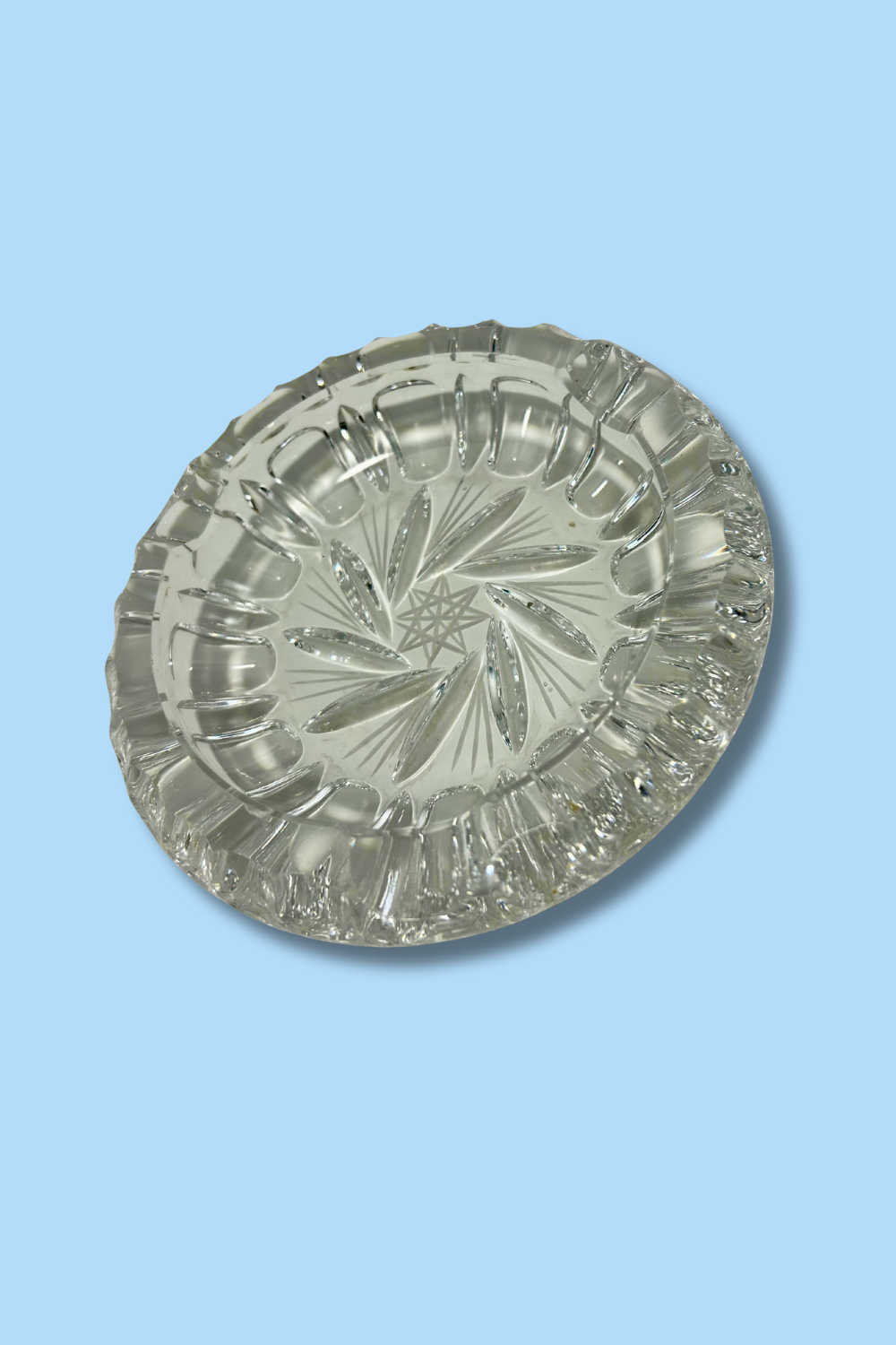 Clear crystal ashtray with Hob Star and pinwheel pattern on a light blue background