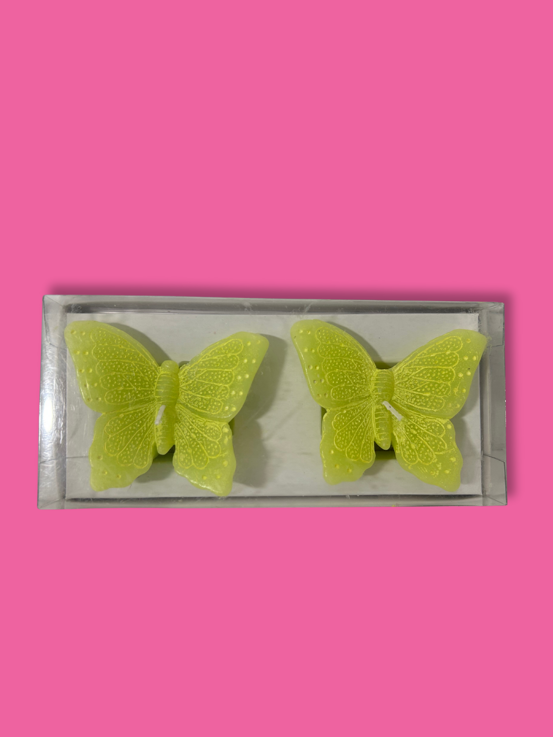 Two lime green butterfly shaped candles on a pink background