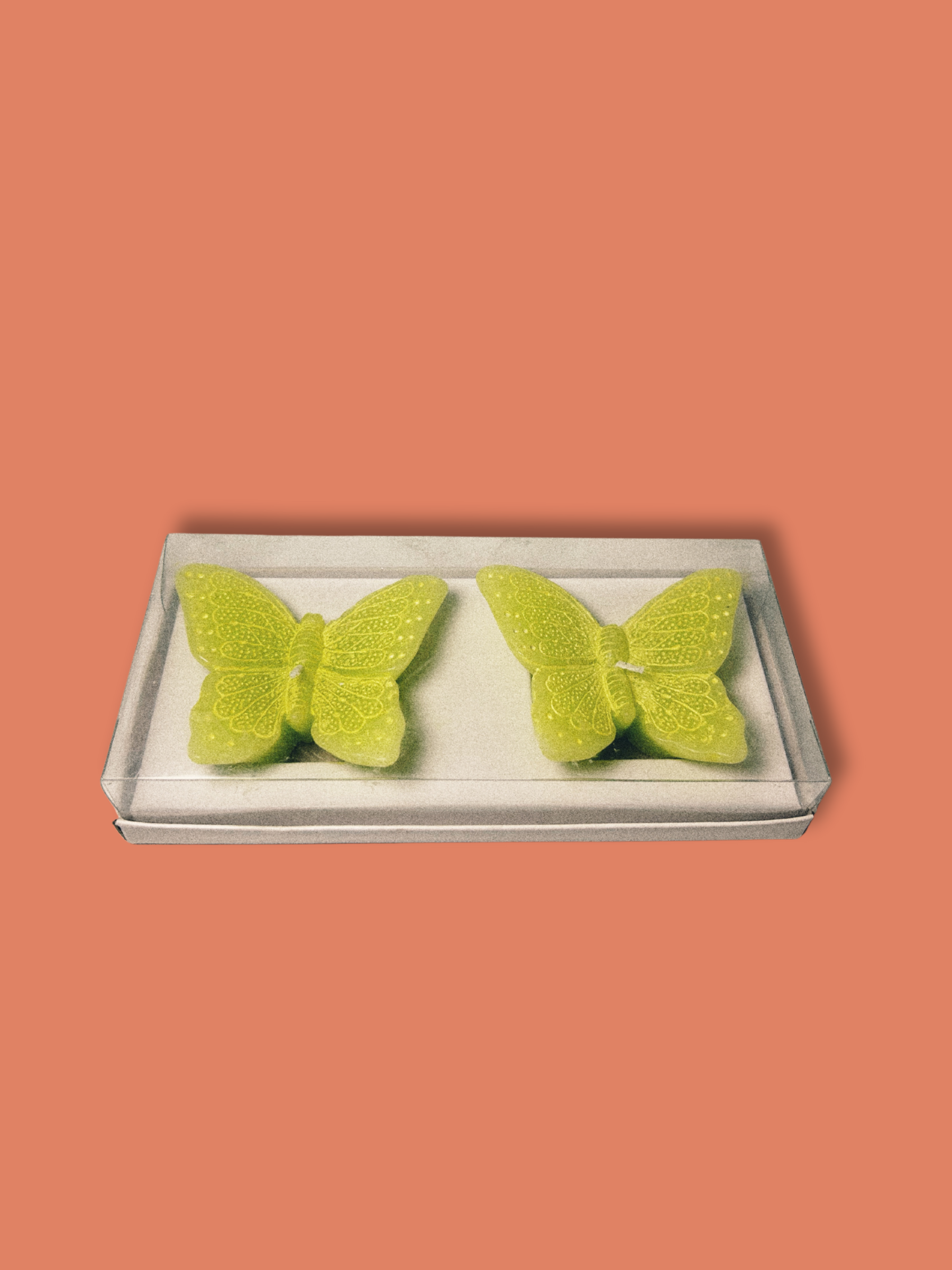 Two lime green butterfly shaped candles on an orange background