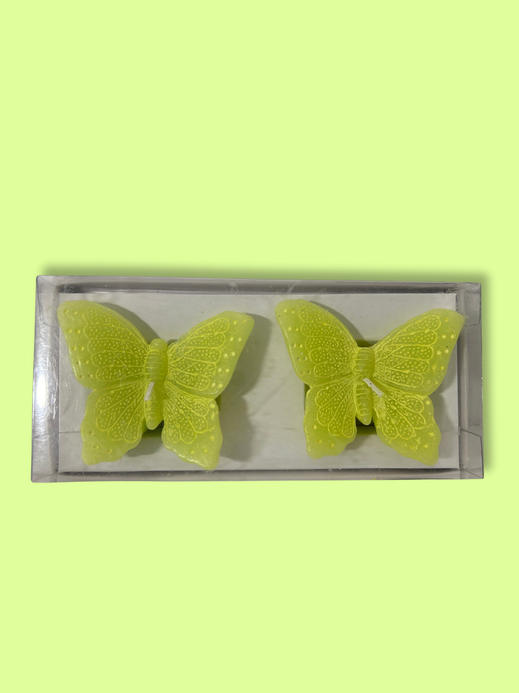 Two lime green butterfly shaped candles on a green background