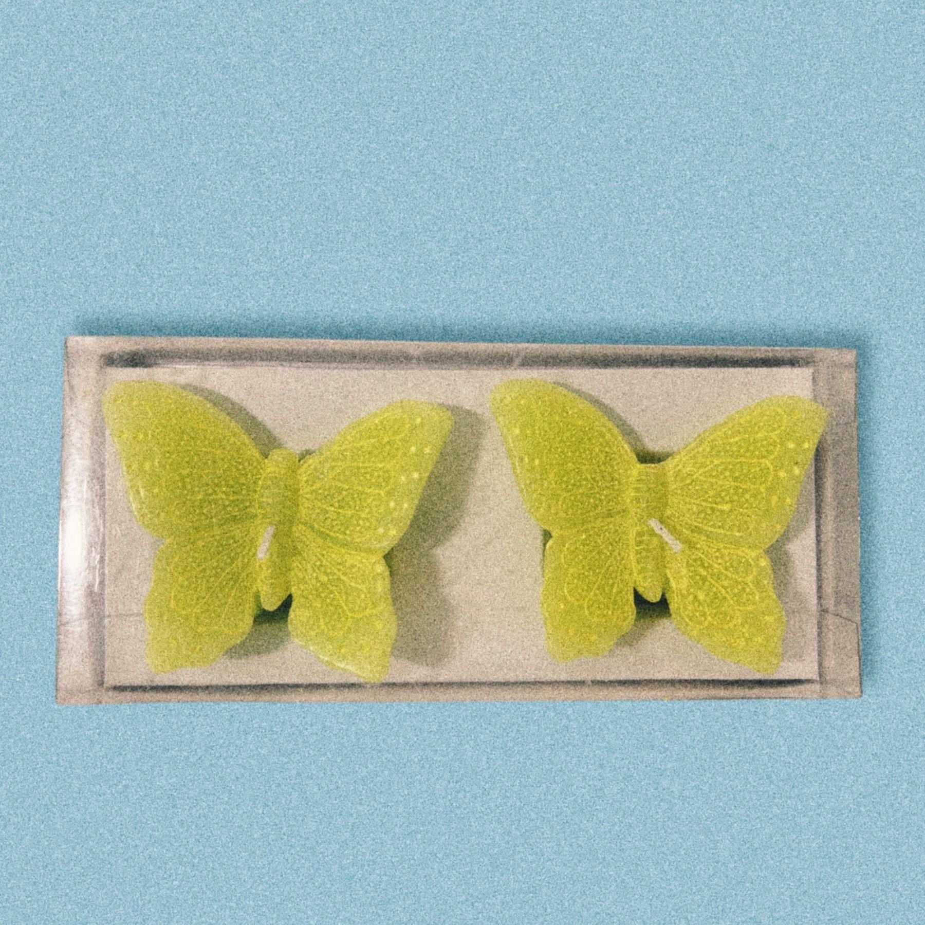 Two lime green butterfly shaped candles on a blue background