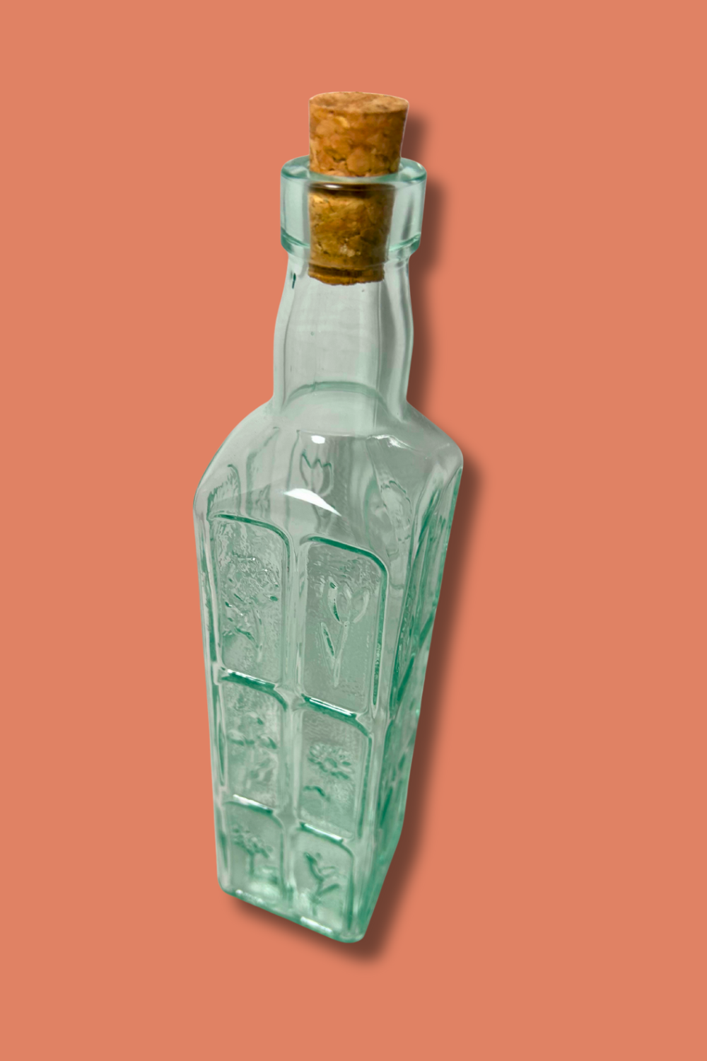 Green glass bottle with cork on a peach background