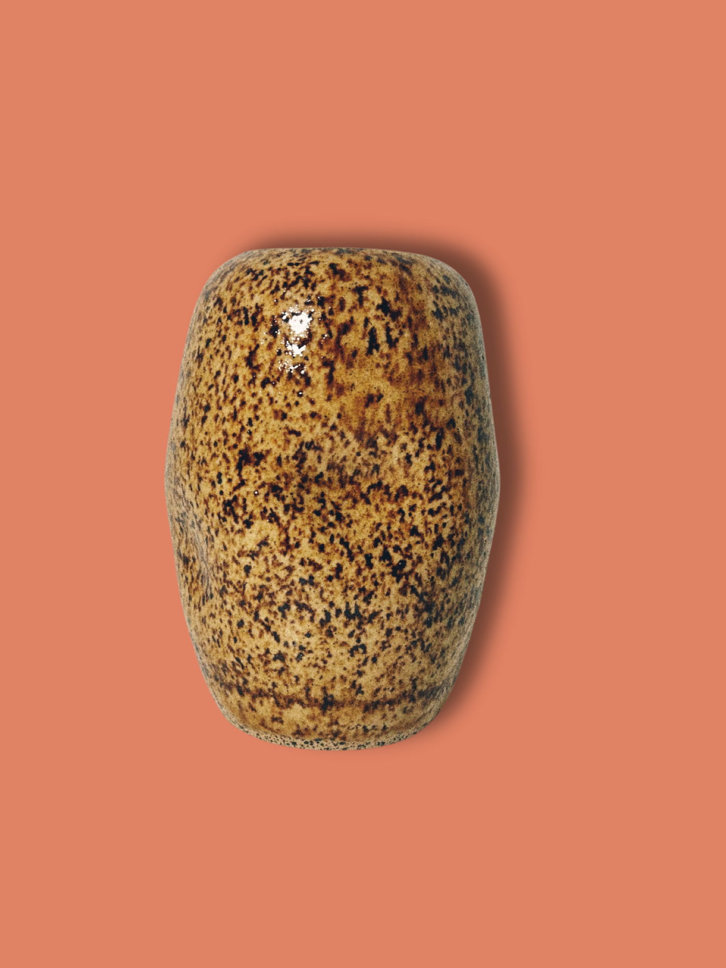 A handmade ceramic brown speckled jar on an orange background.