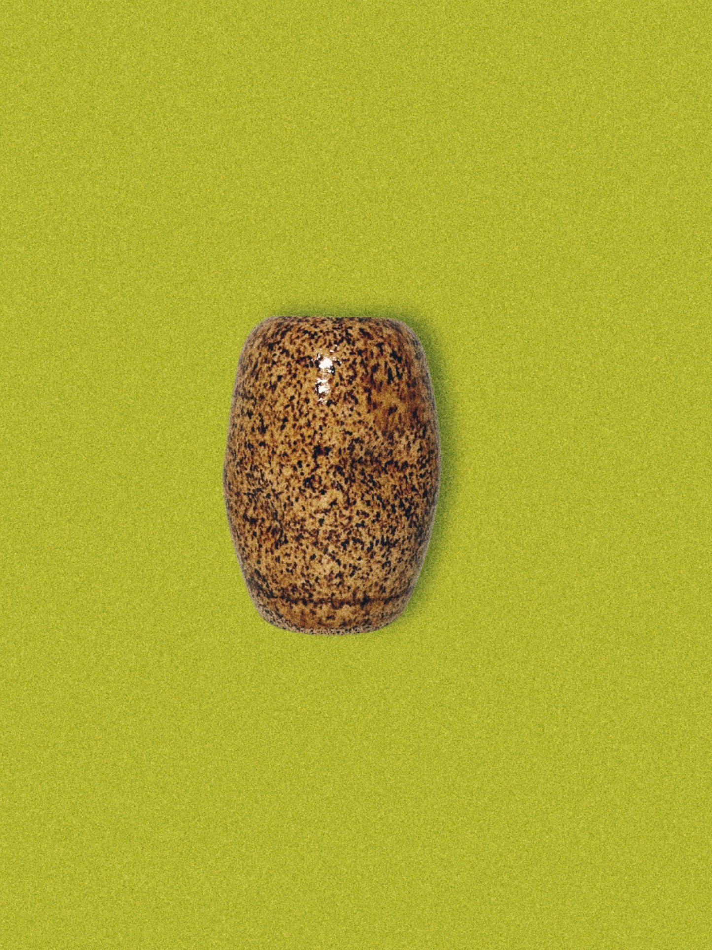 A handmade ceramic brown speckled jar on a green background.
