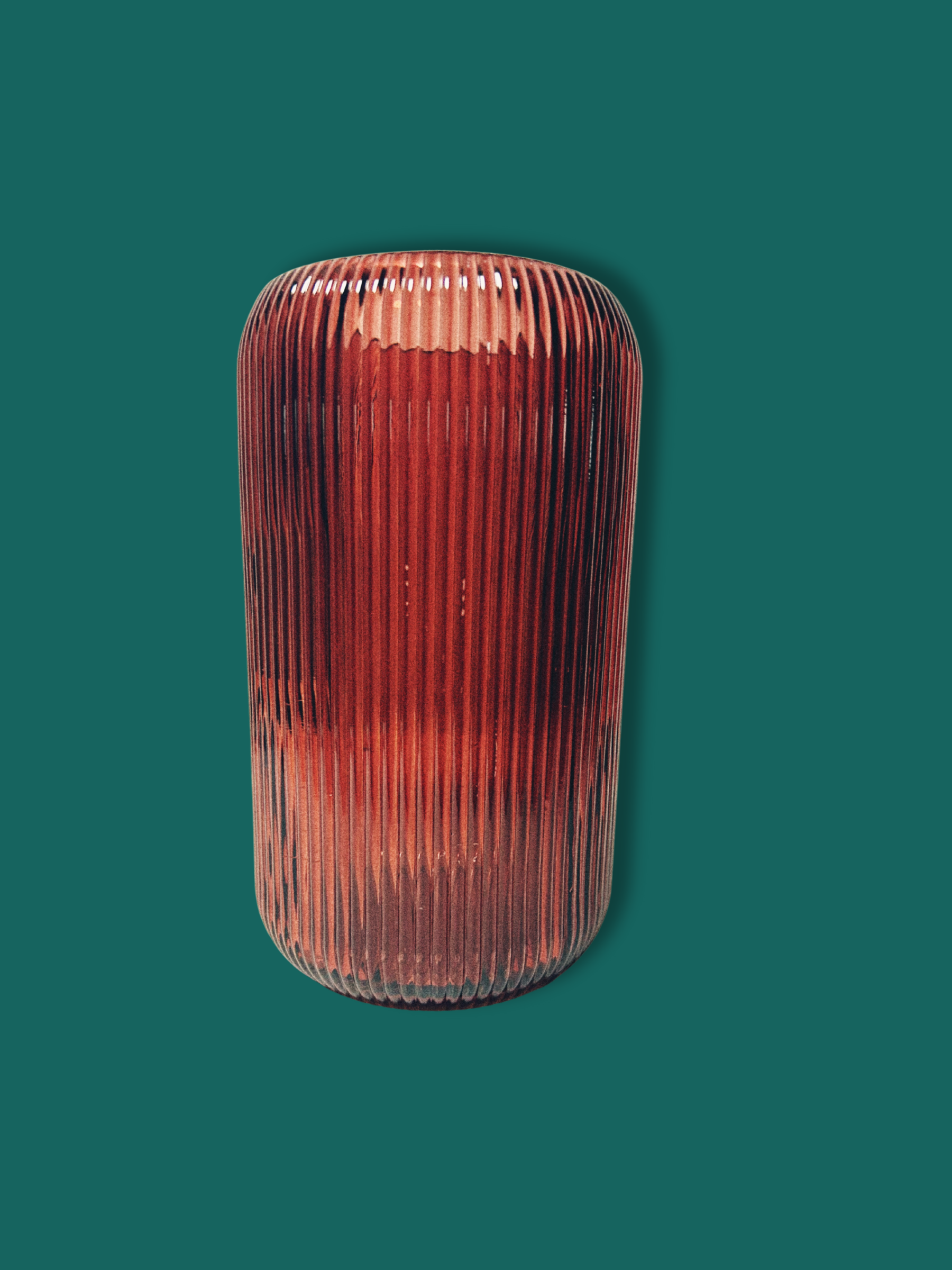 A cylindrical maroon glass vase with vertical ridges against a teal background