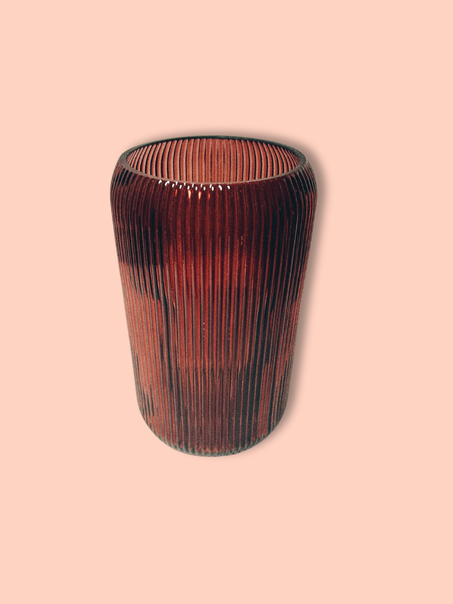 A cylindrical maroon glass vase with vertical ridges against a pink background