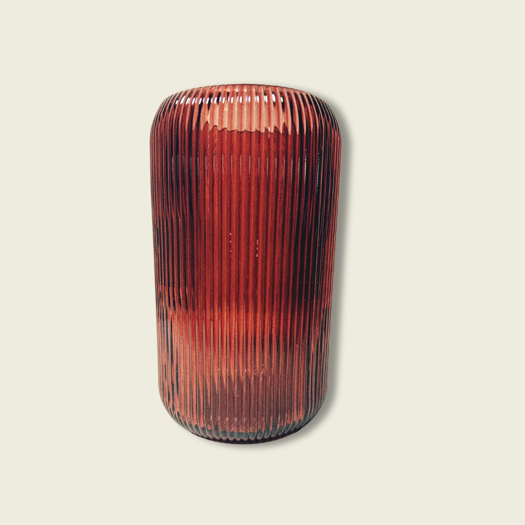 A cylindrical maroon glass vase with vertical ridges against a white background