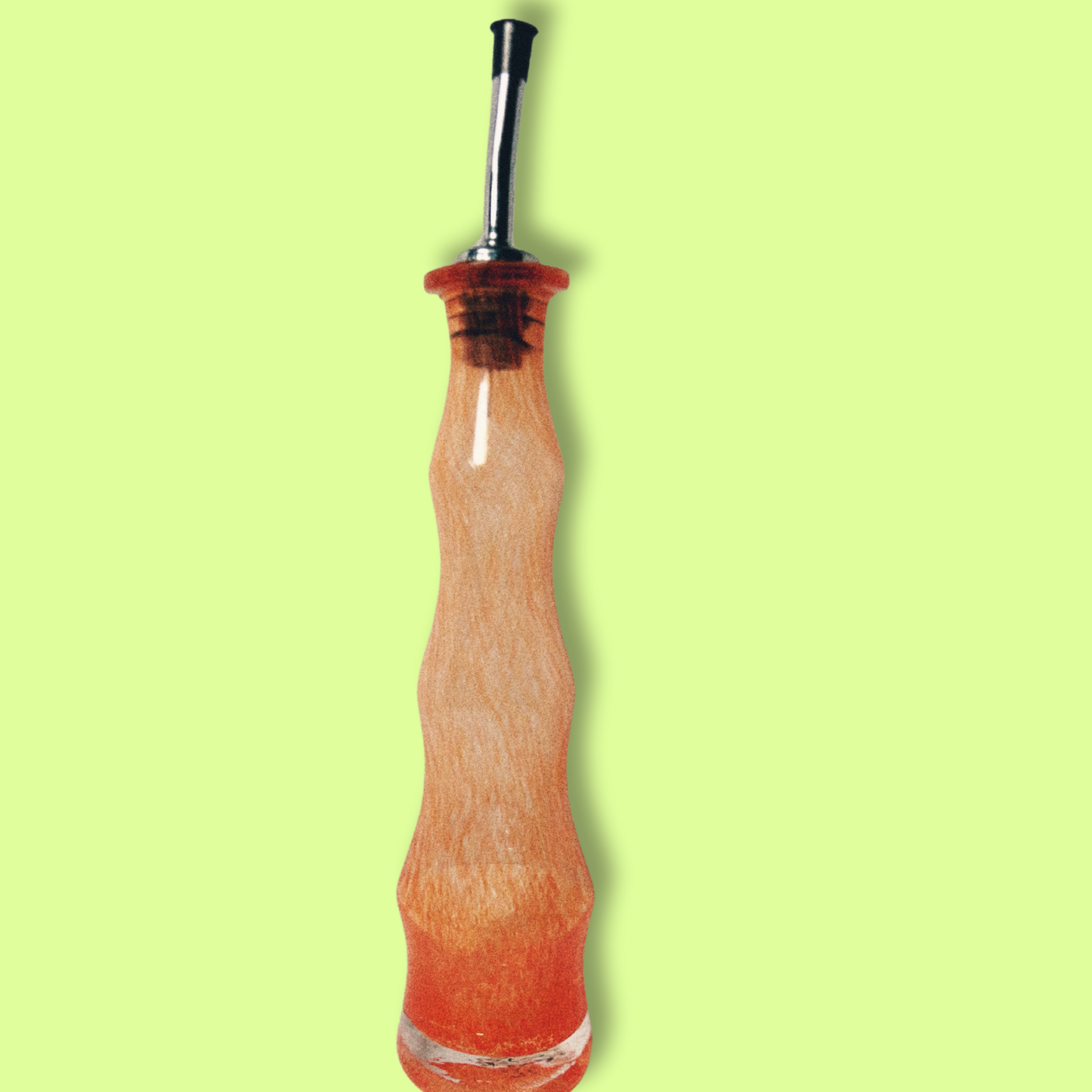 A clear handblown glass olive oil cruet with an orange tint against a bright green background.