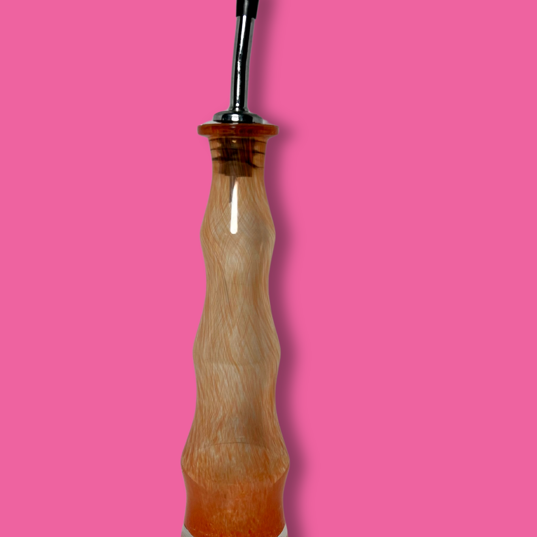 A clear handblown glass olive oil cruet with an orange tint against a bright pink background.