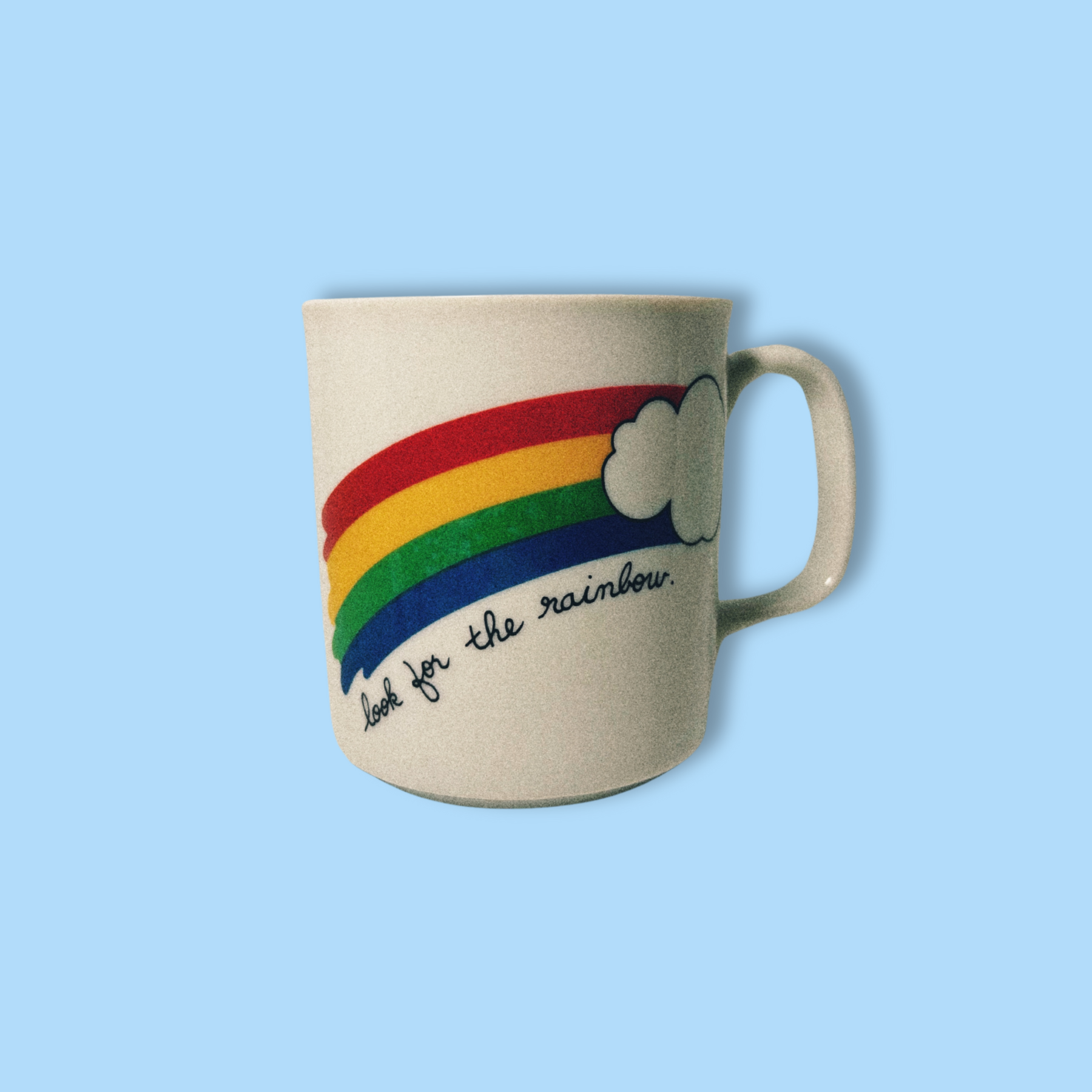 A beige ceramic mug with a colorful rainbow design and the phrase 'look for the rainbow' printed on it.