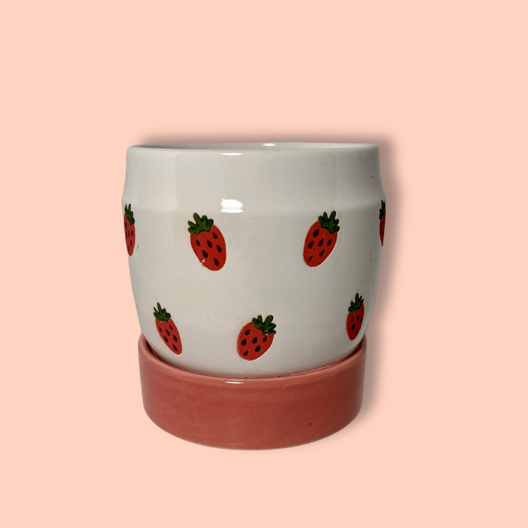 A handpainted ceramic planter with strawberries design on a white background with a pink base.