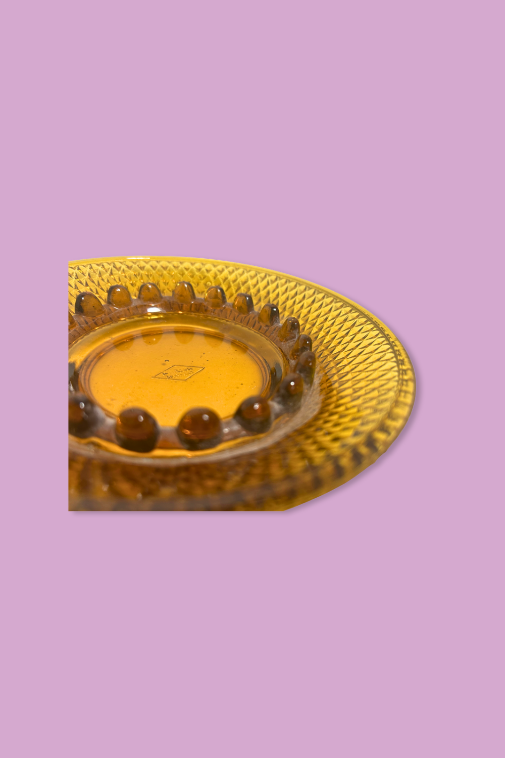 Decorative glass plate with textured rim and central yellow disc on a purple background