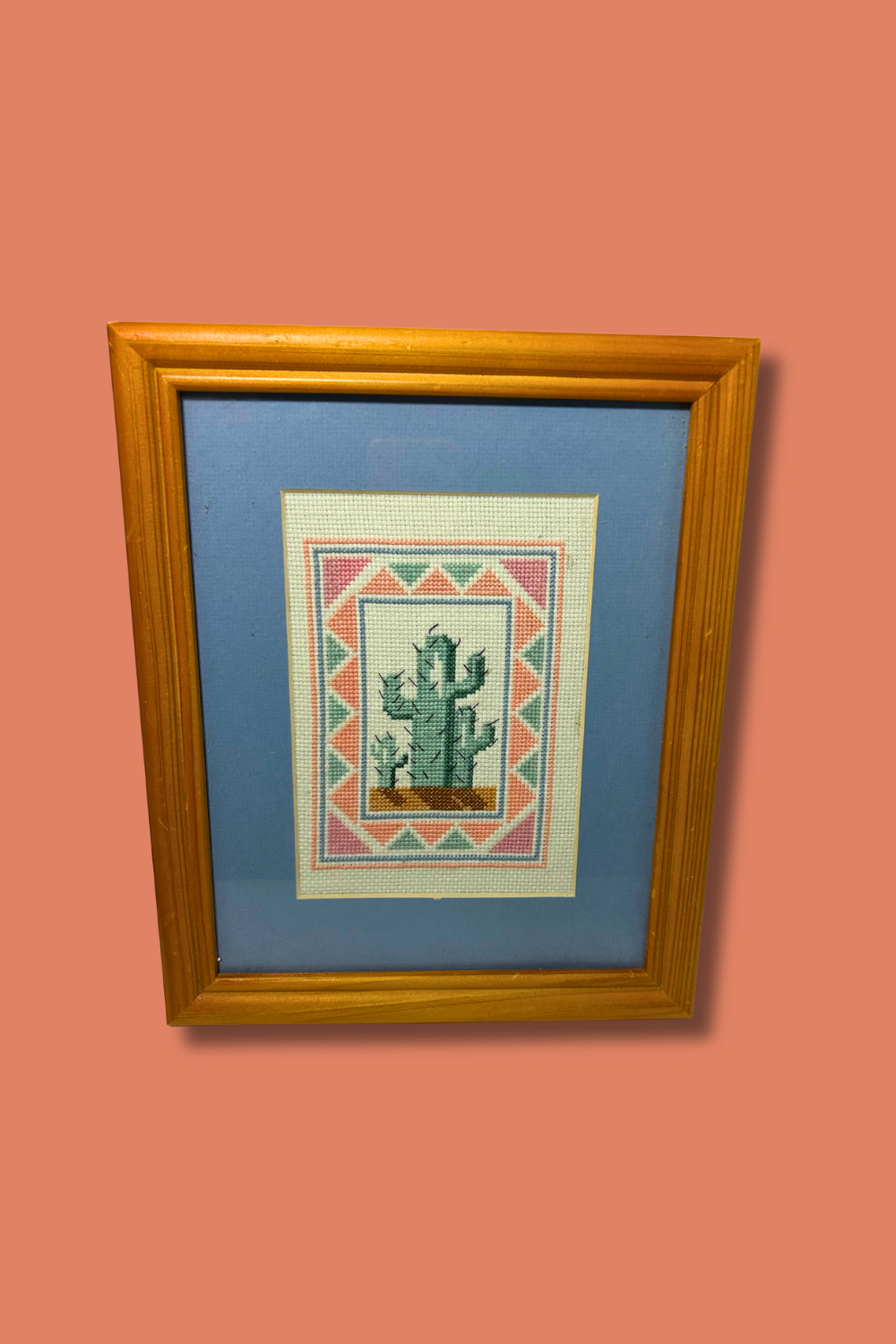 Framed cross-stitched picture of a cactus on a pink wall