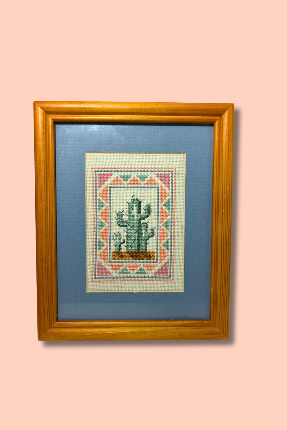 Framed cross-stitched picture of a cactus on a pink background
