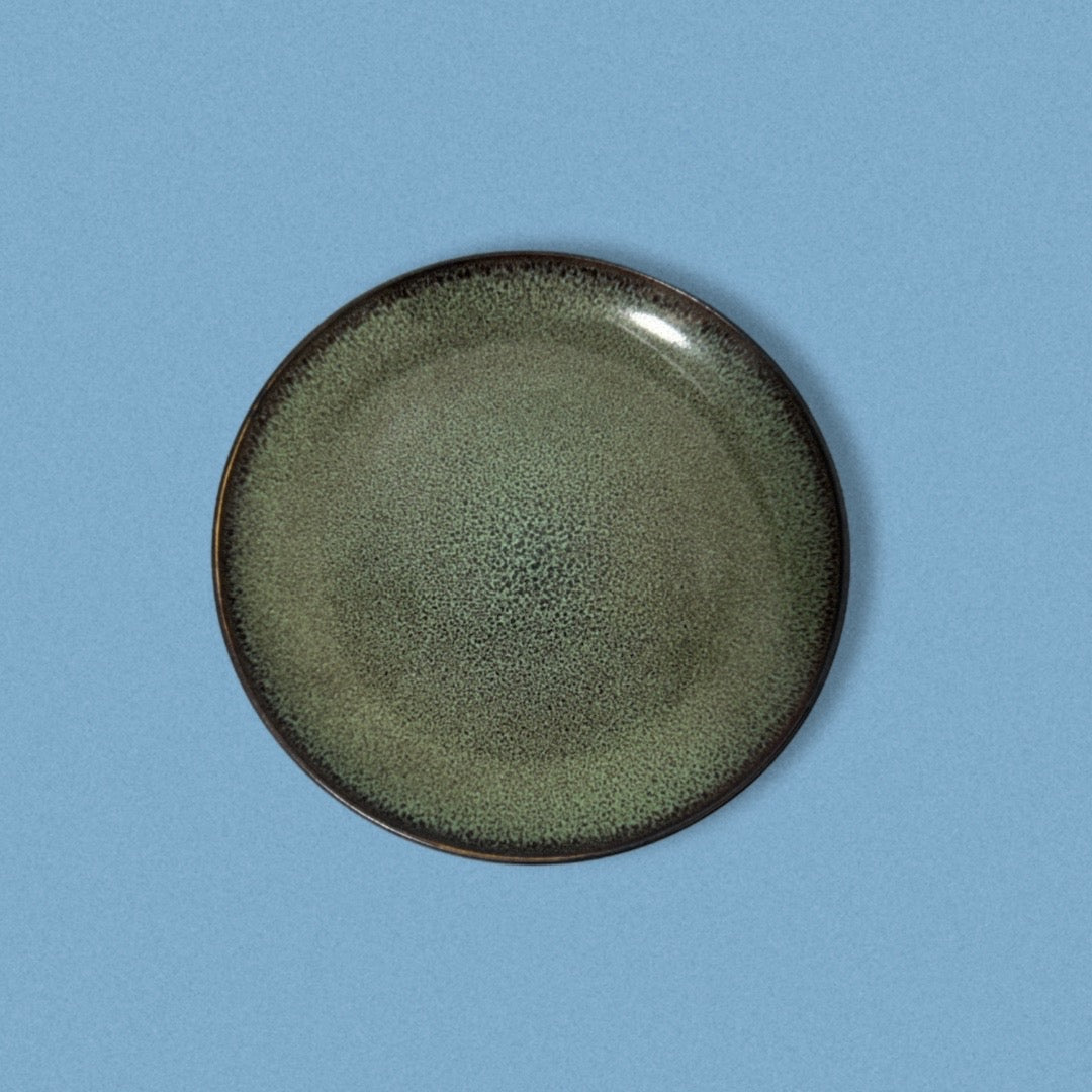 A green salad plate with a textured surface and black rim, displayed on a blue background.