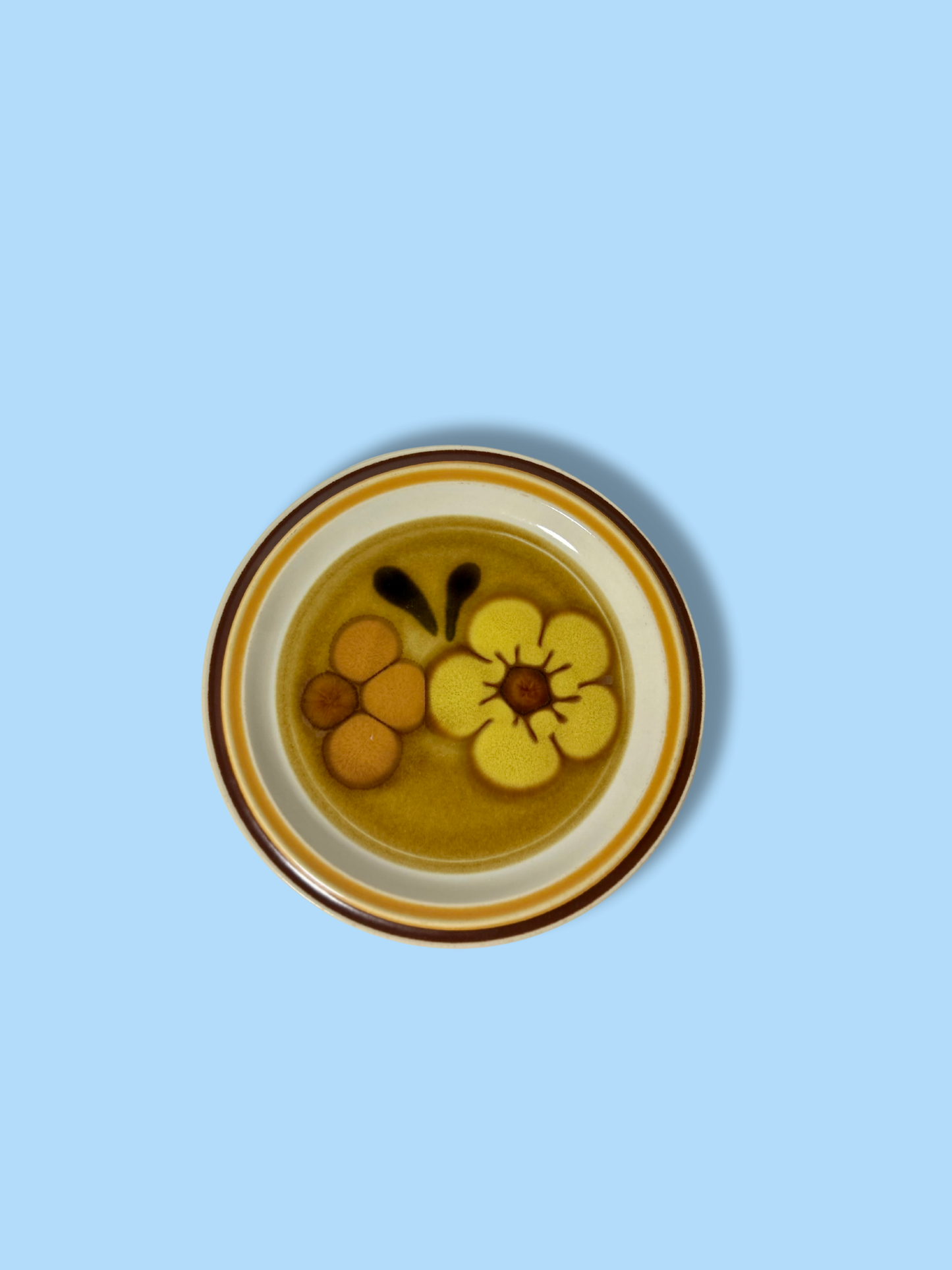 A vintage salad plate with a floral pattern in yellow, orange, and black colors, with a white rim.