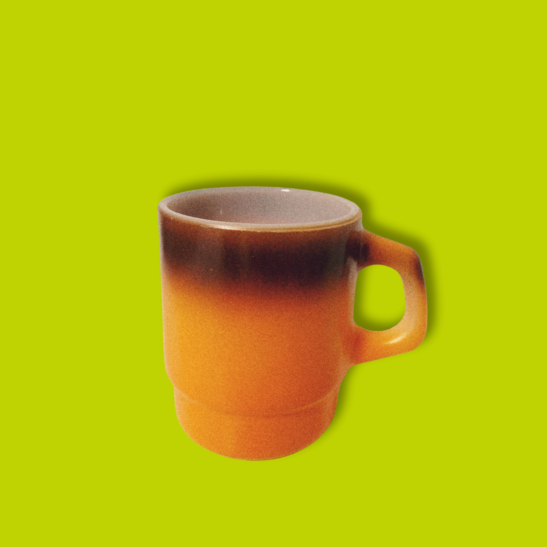 A vintage Anchor Hocking Fire King orange ombre coffee mug against a green background.
