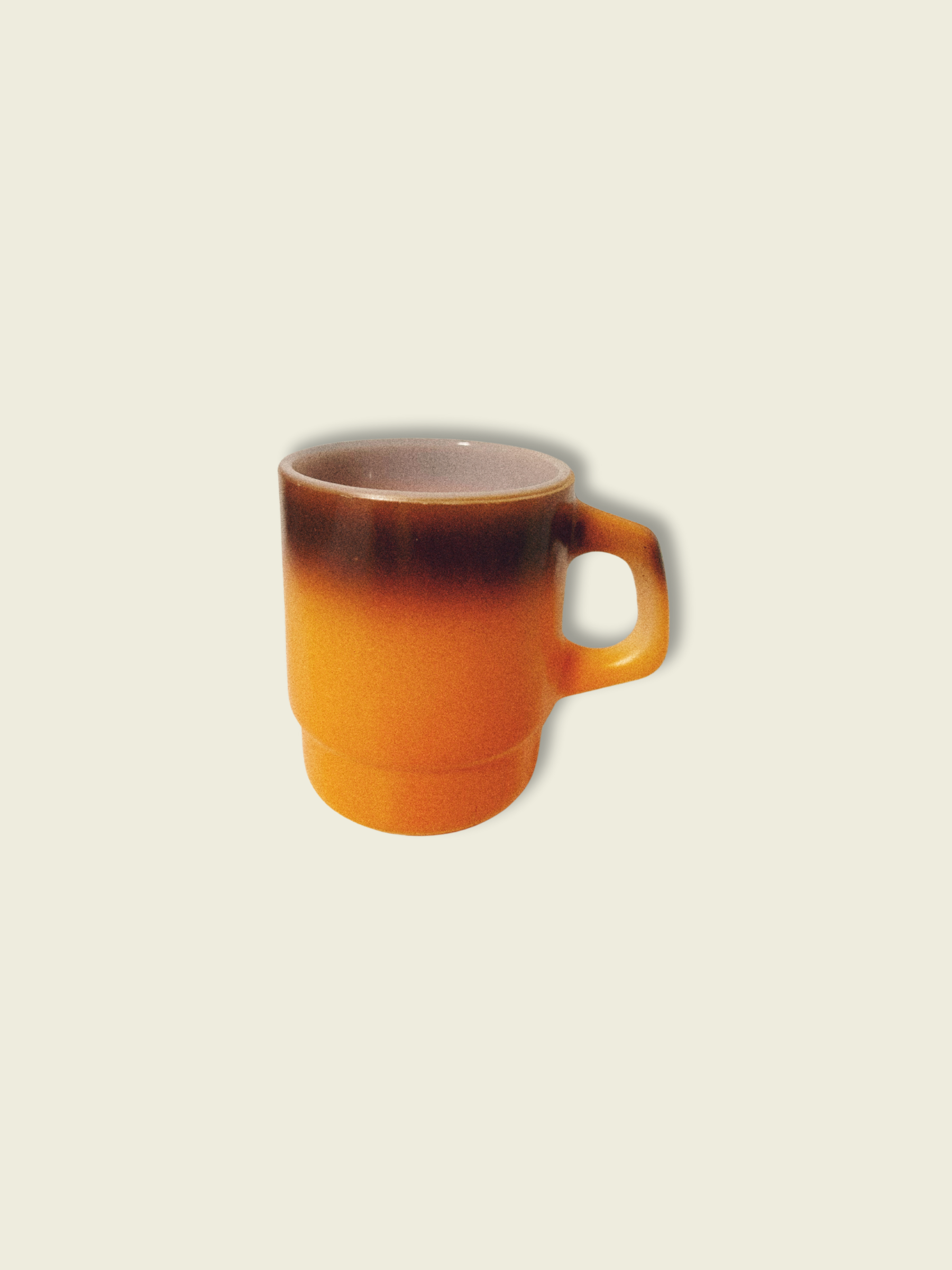 A vintage Anchor Hocking Fire King orange ombre coffee mug against a beige background.