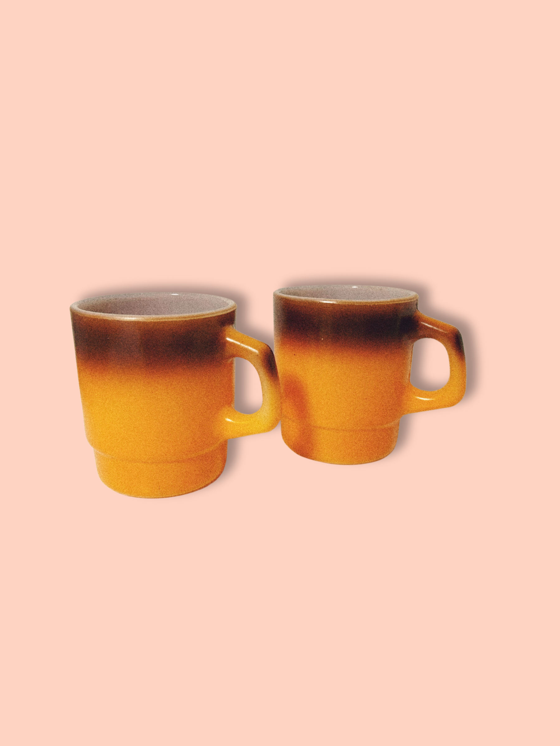 A vintage Anchor Hocking Fire King orange ombre coffee mug against a pink background.