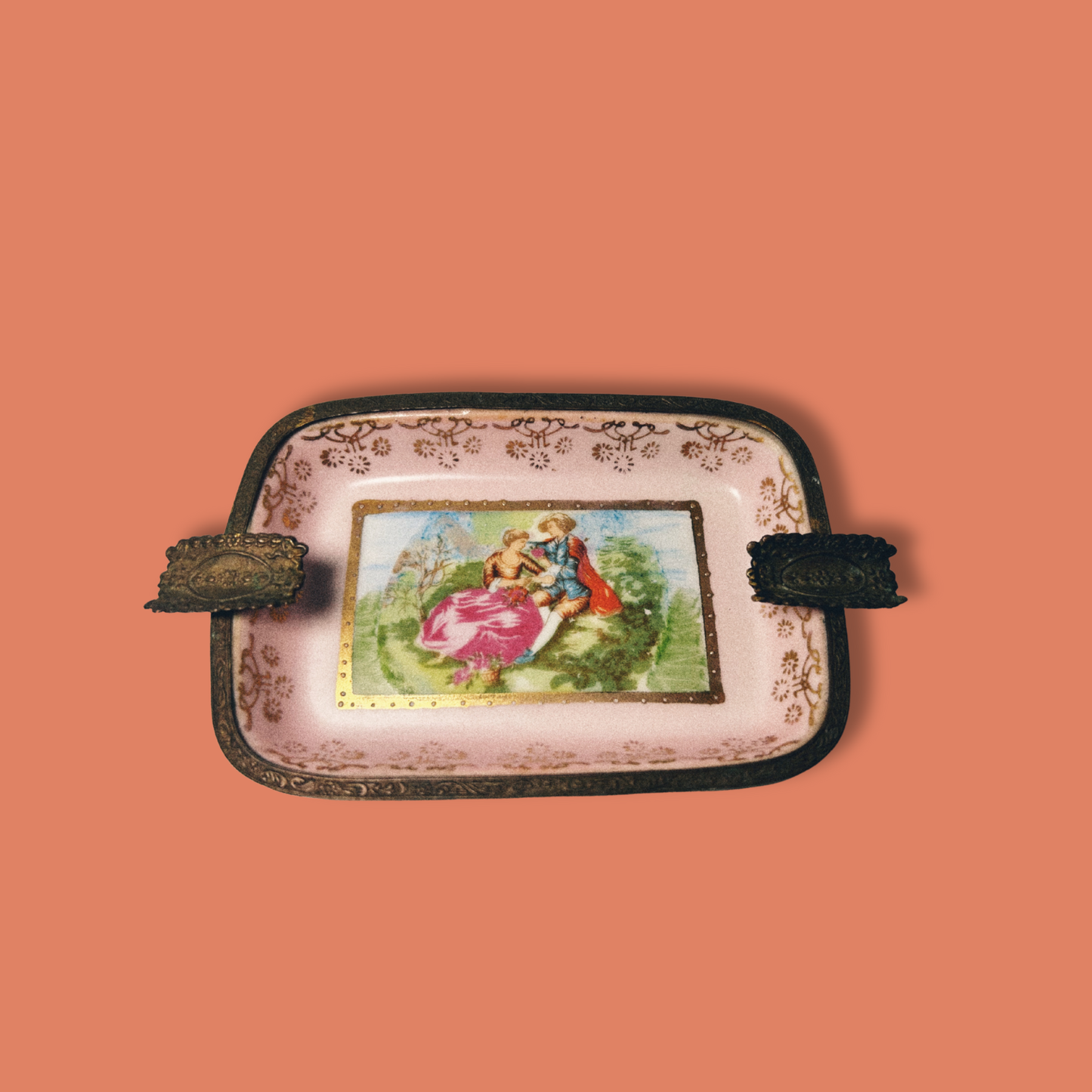 A vintage handpainted porcelain ashtray with brass accents and a floral design, featuring a central picture of a woman.