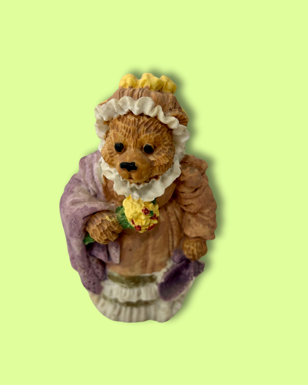 Bear figurine in a vintage dress holding flowers on a light green background