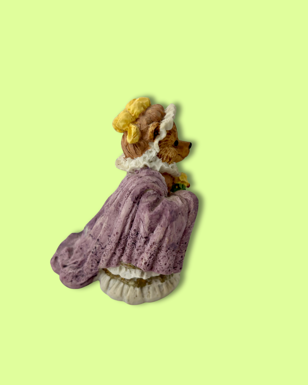 Bear figurine in a purple dress with white lace on a light green background