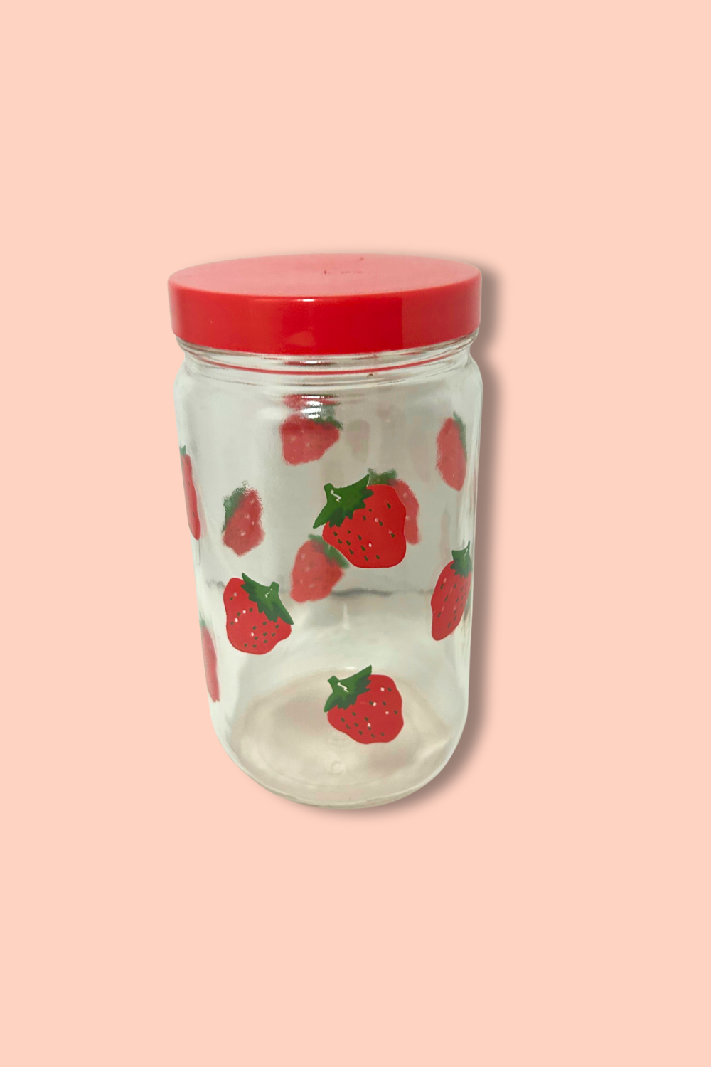 Clear glass jar with red lid and strawberry pattern on a pink background