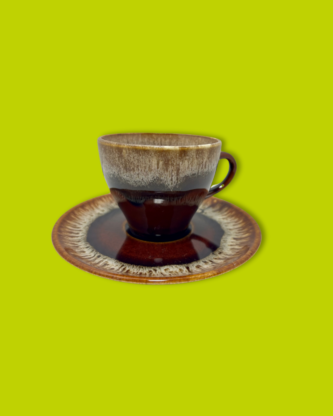 A vintage brown drip tea cup placed on its matching saucer against a green background.