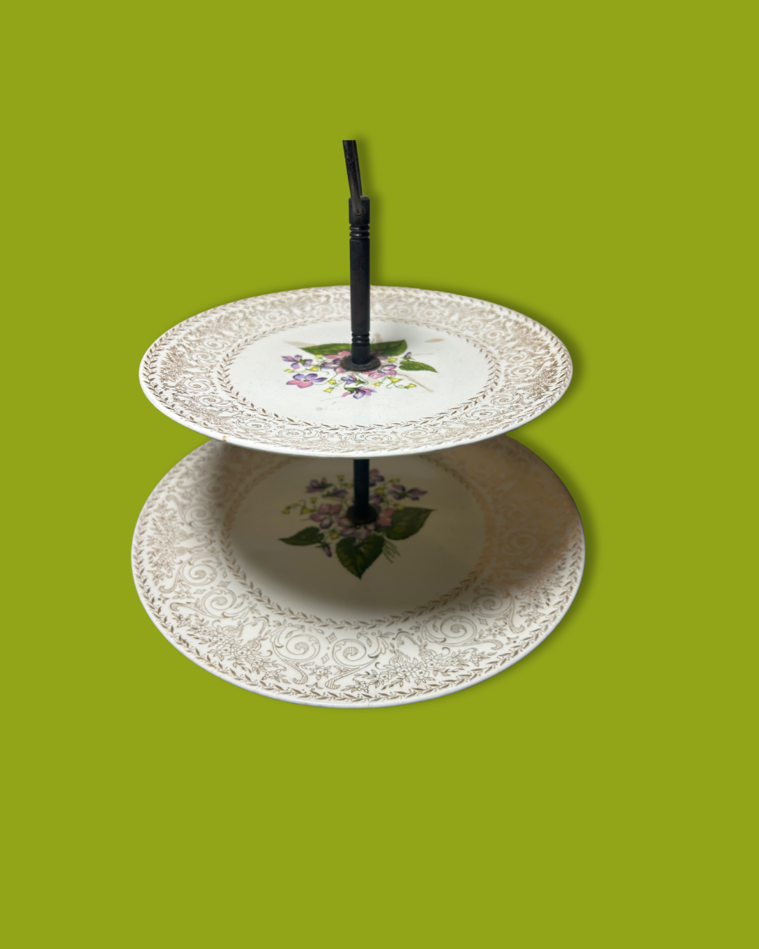 Two-tiered ceramic cake stand with floral design on a green background