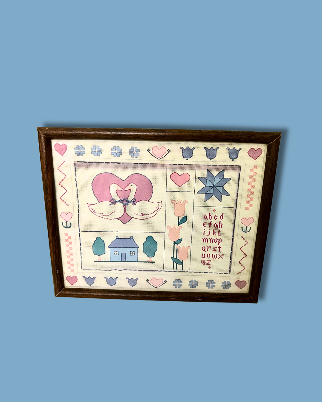 Framed cross-stitched piece with heart design on a blue background