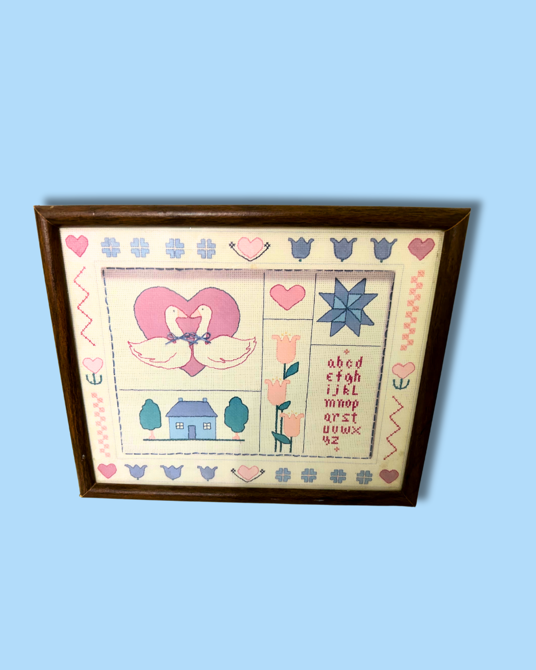 Framed cross-stitched sampler with various patterns and text on a blue background