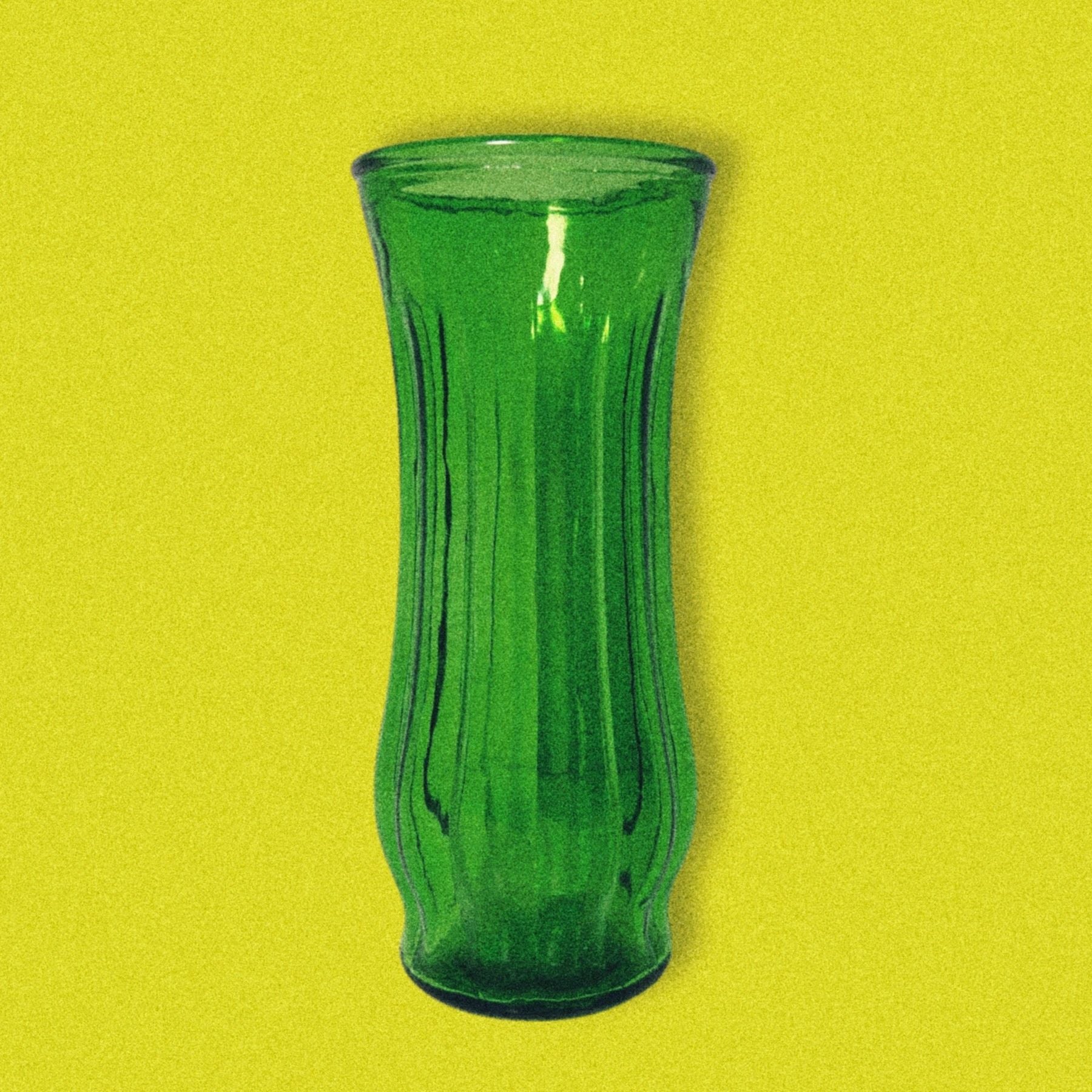 A green glass vase with a ribbed design, displayed against a yellow background.