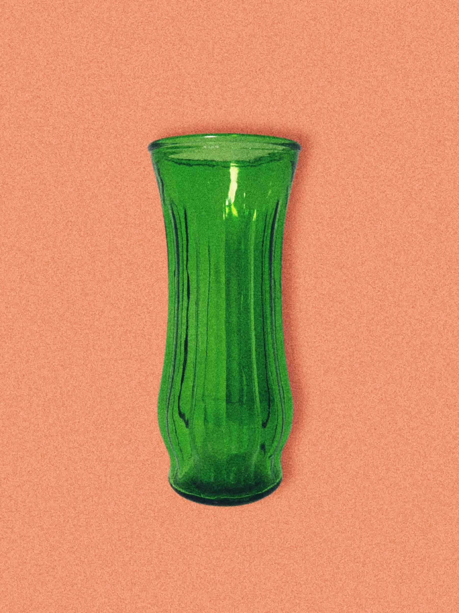 A green glass vase with a ribbed design, displayed against an orange background.
