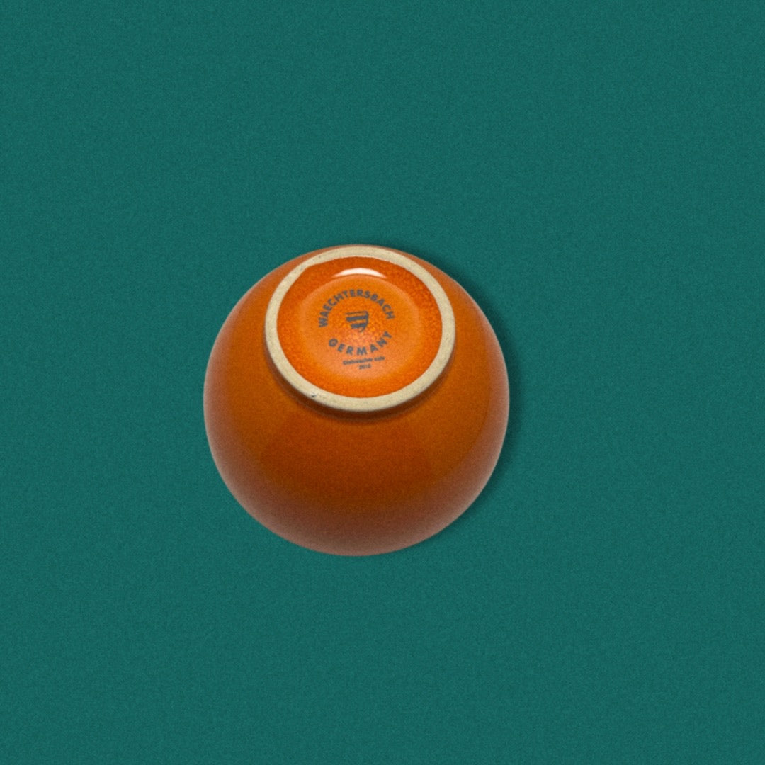 A small orange ceramic bowl with a blue and white striped rim on a green background, viewed from the top.