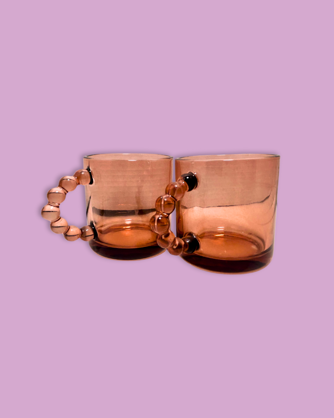 A pair of pink glass mugs with beaded handles on a purple background.
