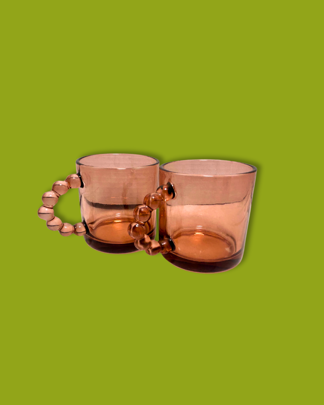 A pair of pink glass mugs with beaded handles on a green background.