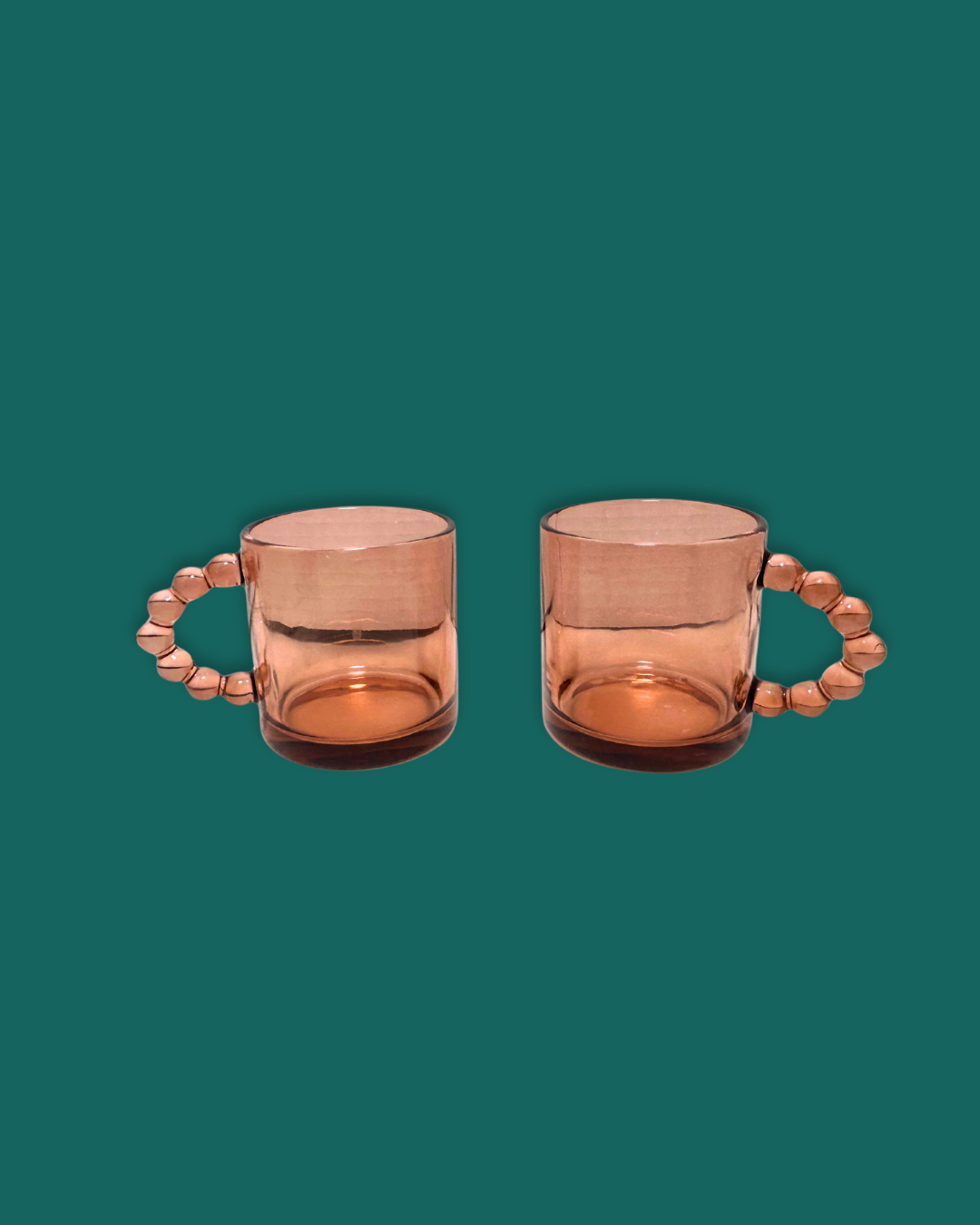 A pair of pink glass mugs with beaded handles on a teal background.