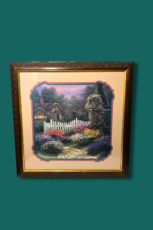 Framed artwork of a garden scene with a white picket fence on a green background