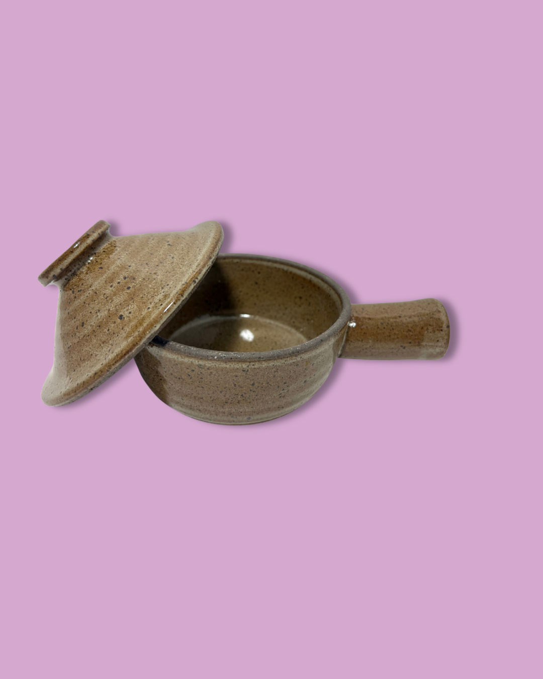 A brown handmade ceramic soup crock with a handle, isolated on a purple background.