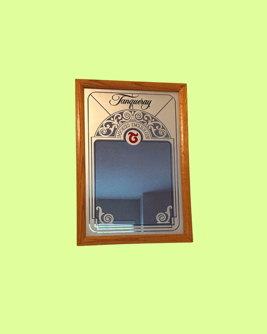 A vintage Tanqueray branded mirror with a decorative wooden frame