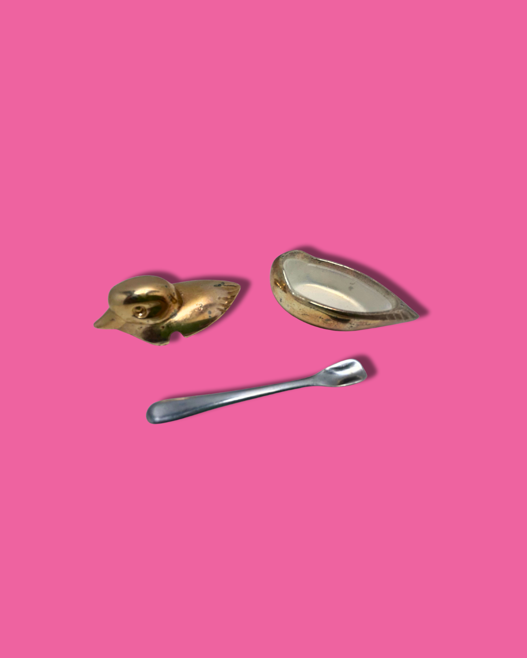 Two gold-colored metal objects and a silver spoon on a pink background