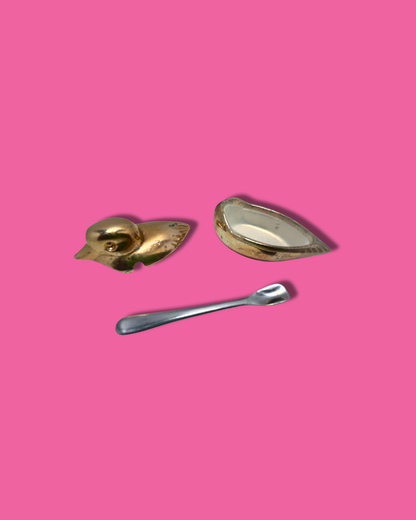 Two gold-colored metal objects and a silver spoon on a pink background