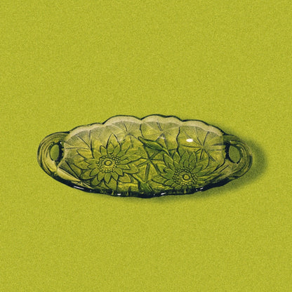 Avocado green glass candy dish with a sunflower pattern on a green background.