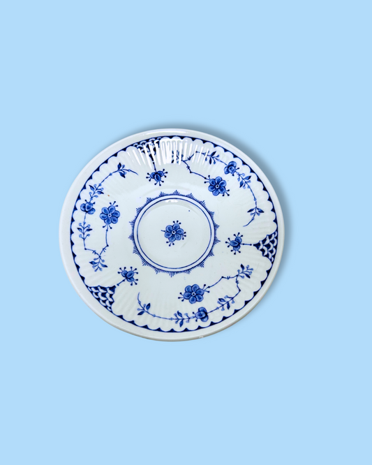 A white ceramic saucer with blue floral patterns and a gold rim on a plain background.