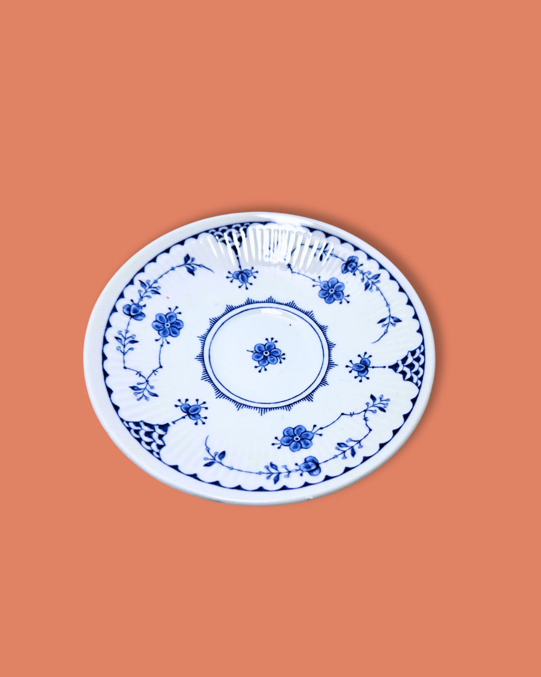 A white ceramic saucer with blue floral patterns and a gold rim on a plain background.