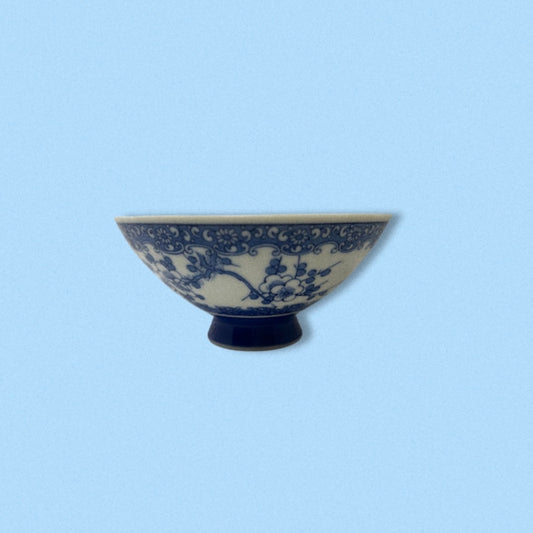 A vintage handpainted blue porcelain Japanese rice bowl with floral patterns on a white background, displayed against a blue background.